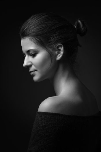 Side view of young woman looking away against black background