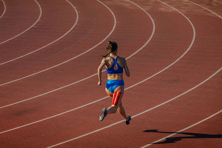 Female athlete running track with kinesio tape on her leg