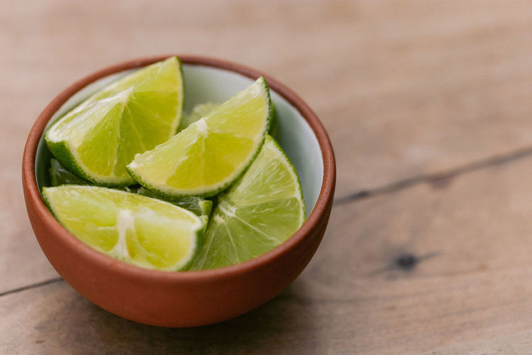 A small bowl of green limes on a wooden table