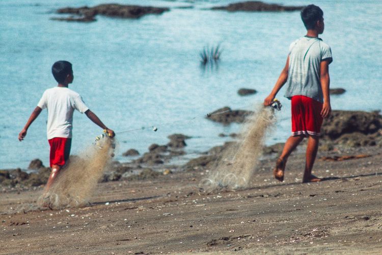 Full length of boy holding fishing net while walking on shore
