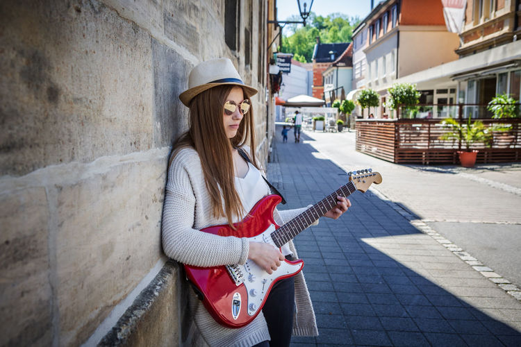Young woman playing guitar while standing by wall