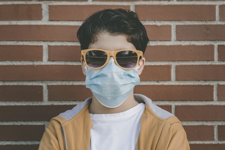 Portrait of boy wearing and mask sunglasses against brick wall