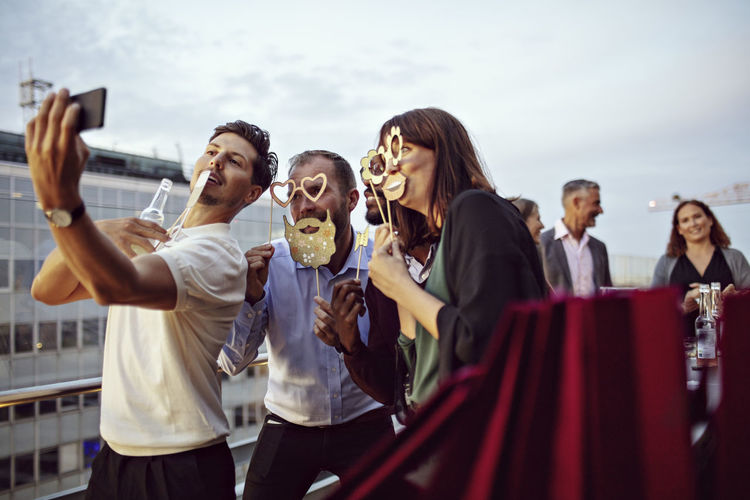 Business colleagues holding props while taking selfies in office celebrations on terrace