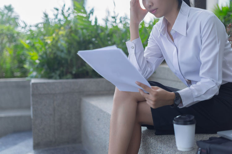 Midsection of stressed businesswoman holding papers while sitting outdoors