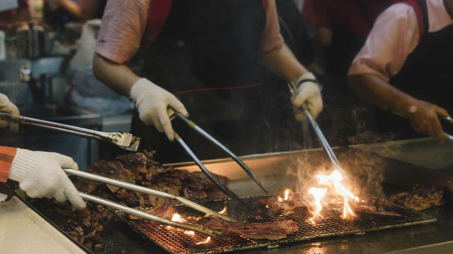 Cropped hands roasting meat on barbecue grill