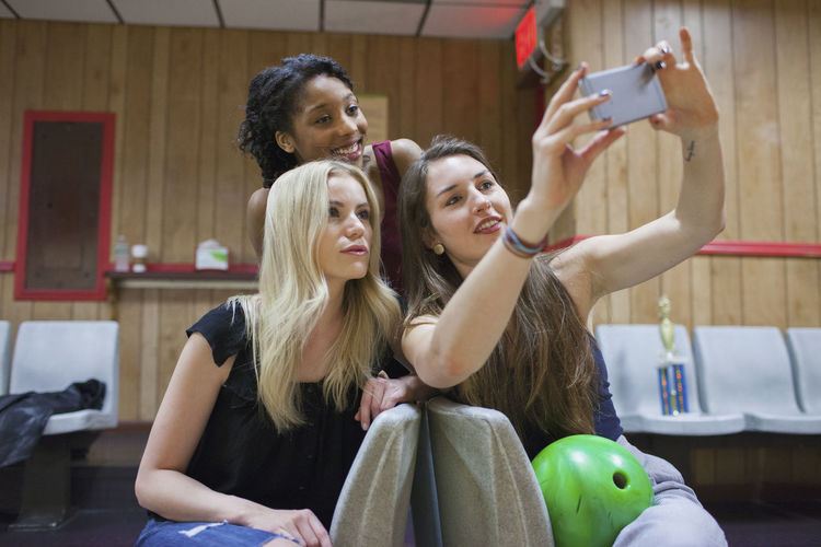 Two young woman taking a picture on a cell phone.