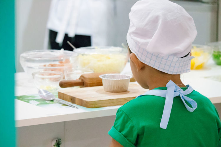 Rear view of boy in chef hat cooking food in kitchen