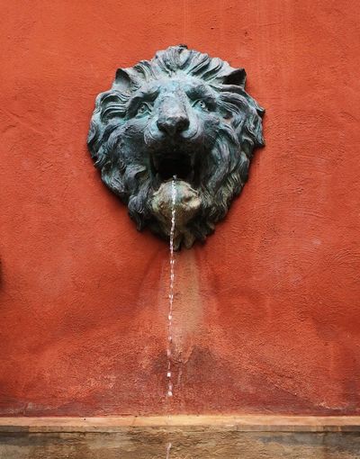 Water dripping from lion shape fountain on brown wall