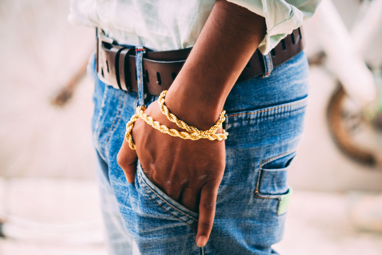 Midsection of man with hands in pocket wearing gold bracelet
