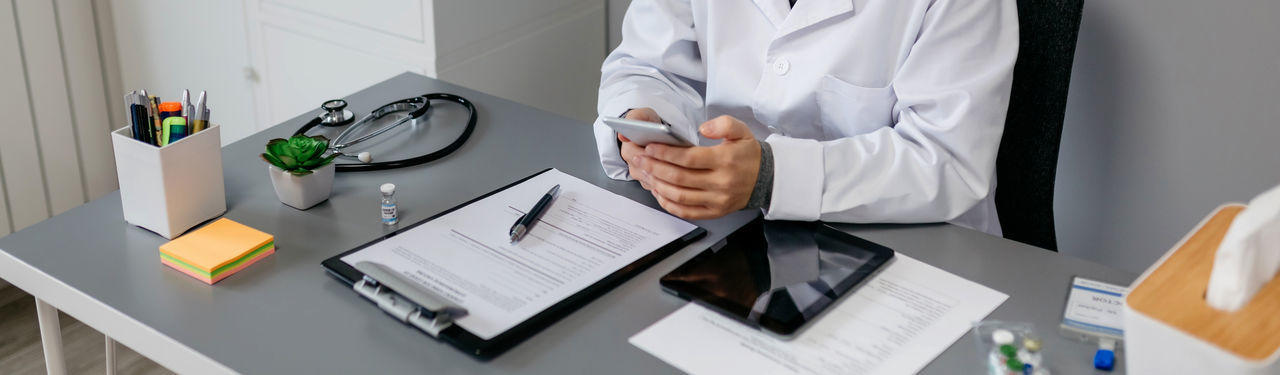 Midsection of doctor using mobile phone at desk