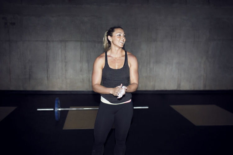 Happy female athlete looking away white chalking hands in gym