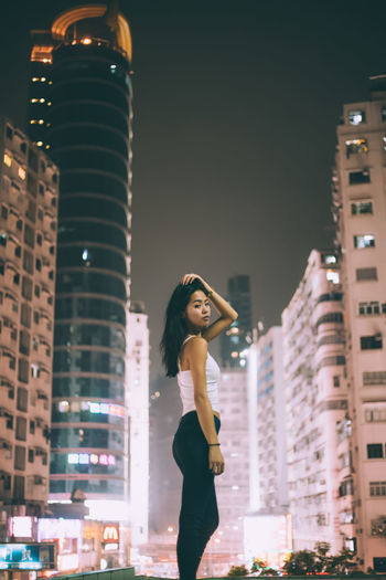 Portrait of beautiful woman standing against illuminated buildings in city at night
