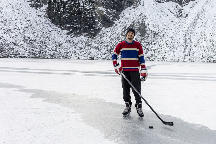 Happy hockey player on frozen lake with stick and puck while smiling