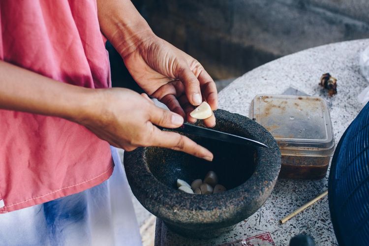 Midsection of woman cutting food in mortar and pestle on table