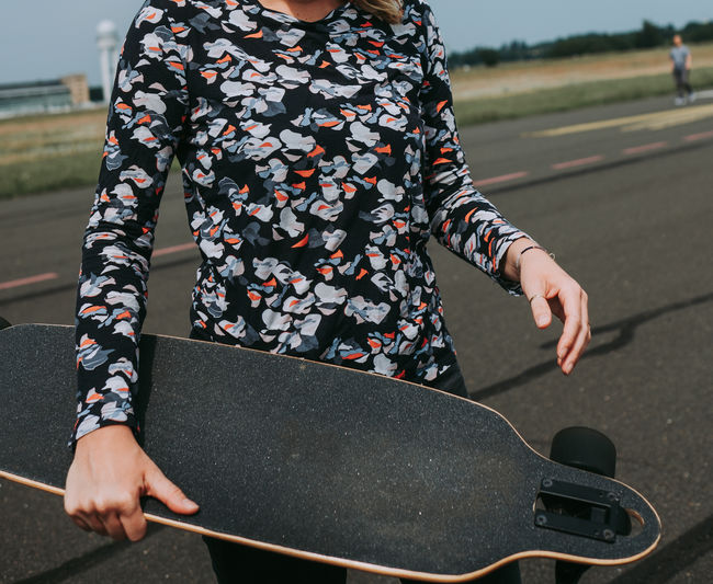 Midsection of woman carrying longboard on road