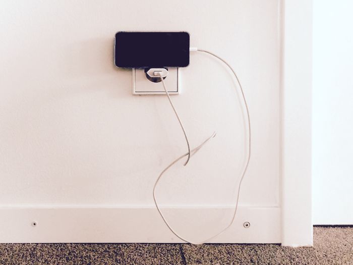 High angle view of smart phone charging against white wall