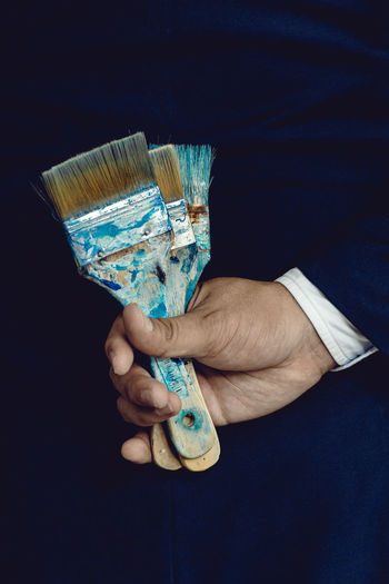 Midsection of man holding brushes against black background