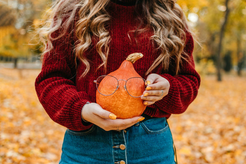 Faceless portrait of woman holding orange halloween pumpkin on autumn park yellow trees background