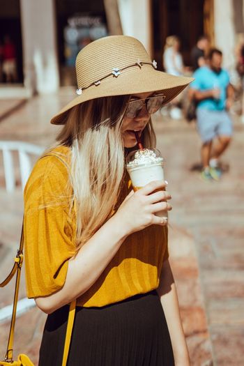 Young woman wearing hat while having cold drink in city during summer