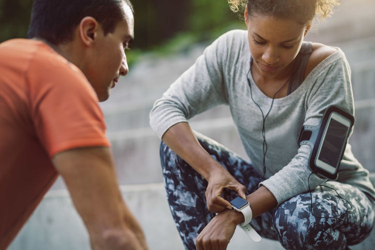Woman looking at smart watch while friend doing push-ups