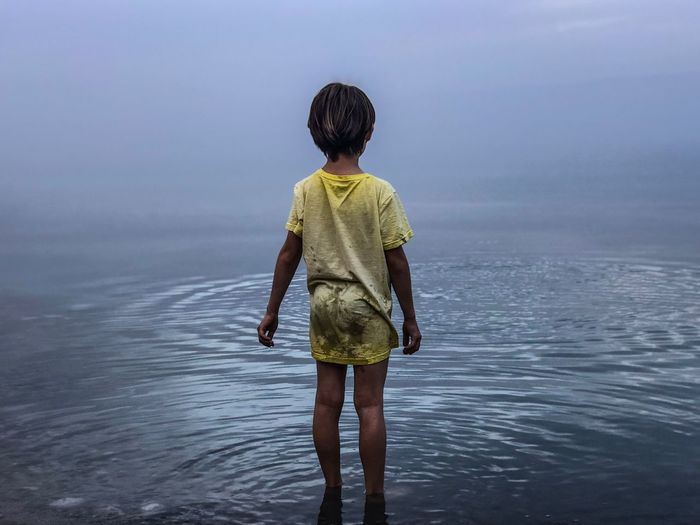 Rear view of boy standing on beach against sky