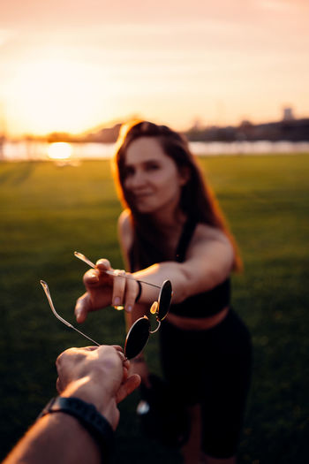 Young woman holding hands on field against sky during sunset