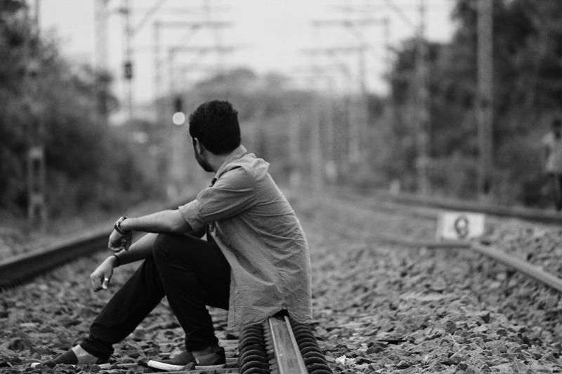 Side view of young man sitting on railroad track