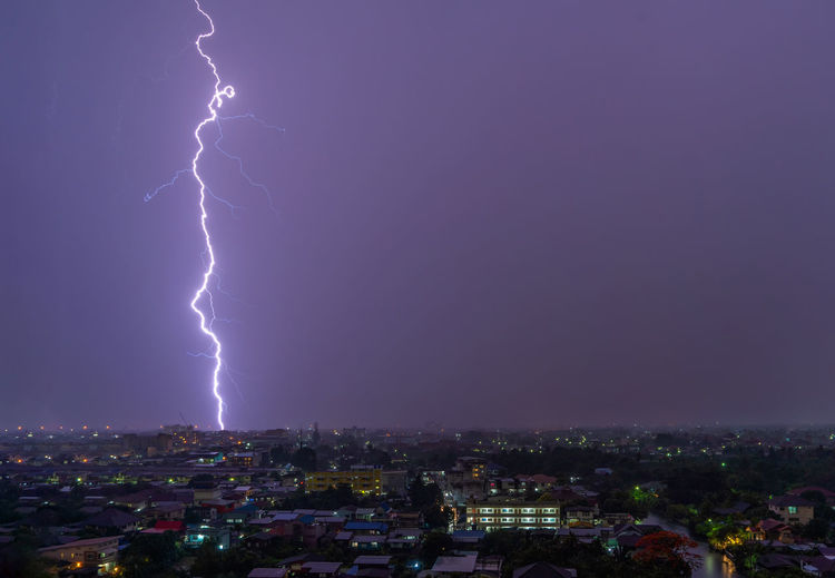 Lightning over illuminated city against sky at night