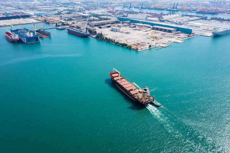 Aerial top view oil ship red tanker and tugboat dragging to shipyard repairing in sea.