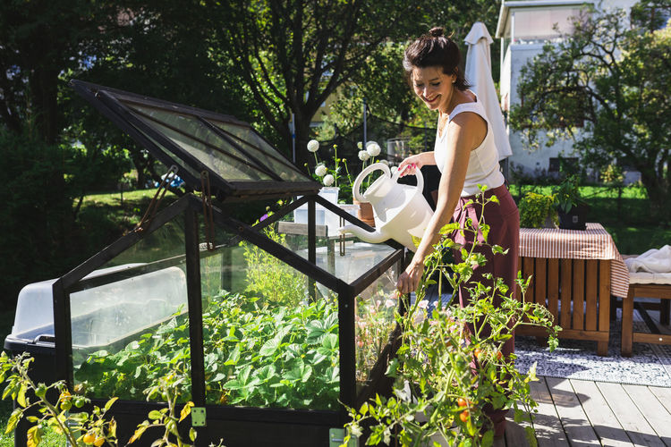 Smiling woman watering plants on terrace