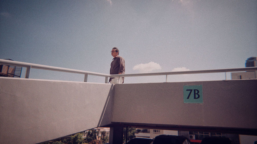 Low angle view of man standing on railing against sky
