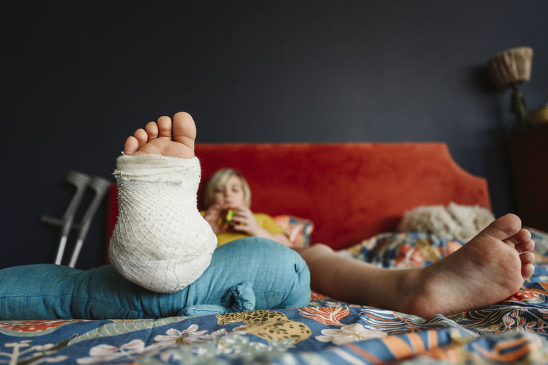 Boy with plaster cast on leg resting on bed at home