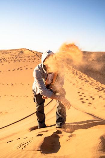 Man playing with sand at desert against clear sky