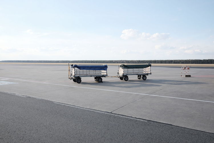 Luggage carts at airport runway against sky
