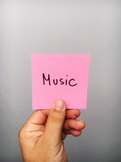 Cropped hand of person holding music text on adhesive note against gray background