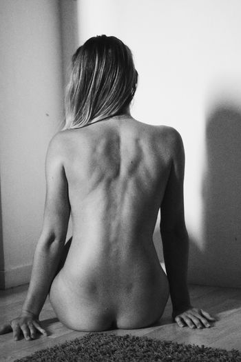 Rear view of shirtless woman sitting against wall
