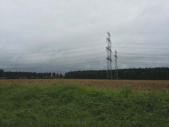 Electricity pylon on field against cloudy sky