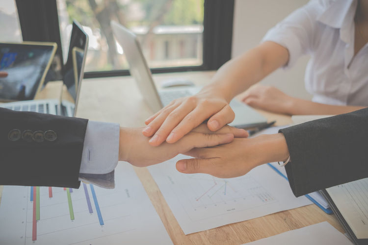 Cropped image of business colleagues huddling hands over table in office