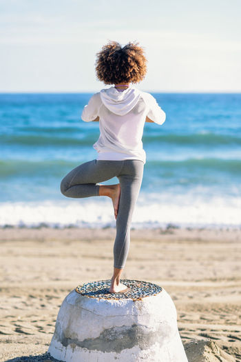 Rear view of woman practicing yoga at beach