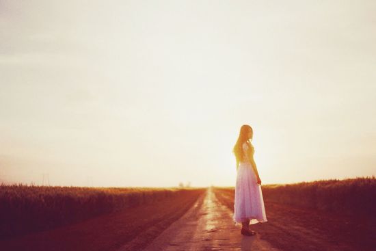 Side view of young woman standing on street against sky during sunset