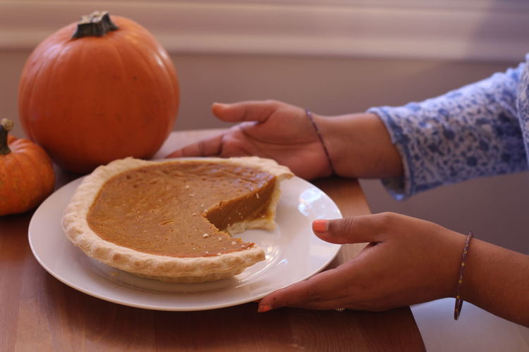Cropped image of woman having pumpkin pie on table