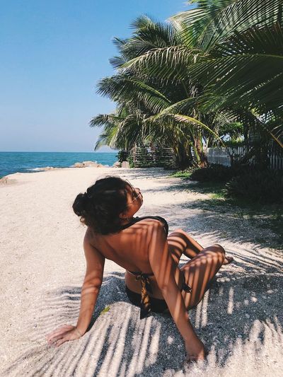 Rear view of woman wearing bikini while sitting at beach