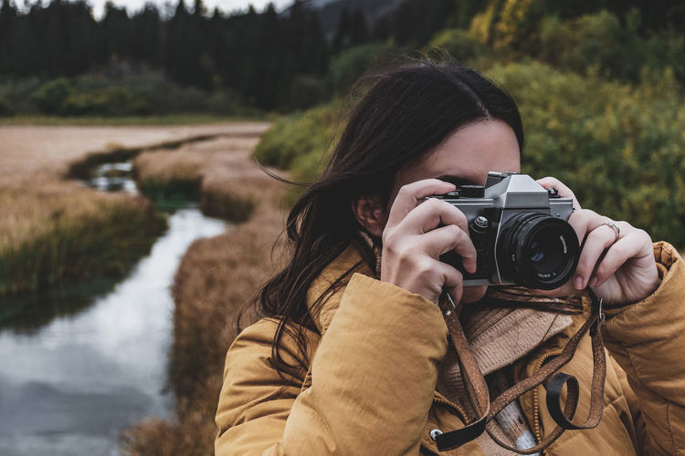 Portrait of young woman taking photos of autumn nature with vintage camera