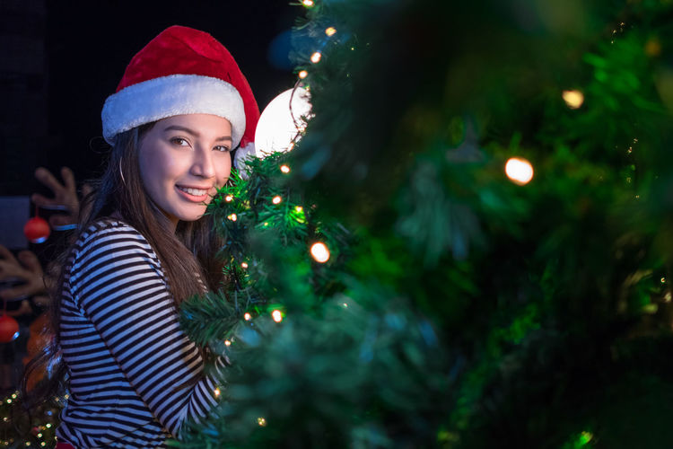 Portrait of smiling woman by illuminated christmas tree at night
