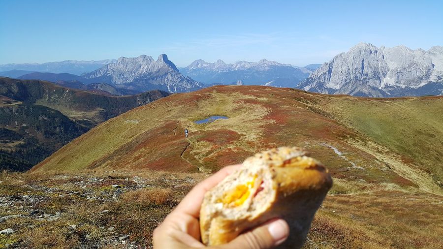 Cropped hand holding burger against mountain
