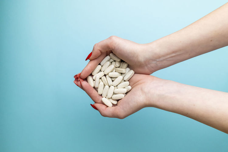 Cropped hands of woman holding pills against blue background