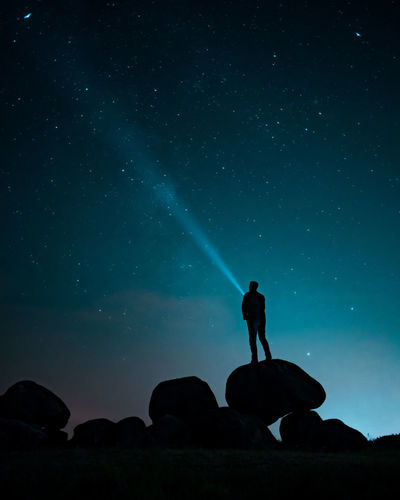 Silhouette man standing on rocks against star field