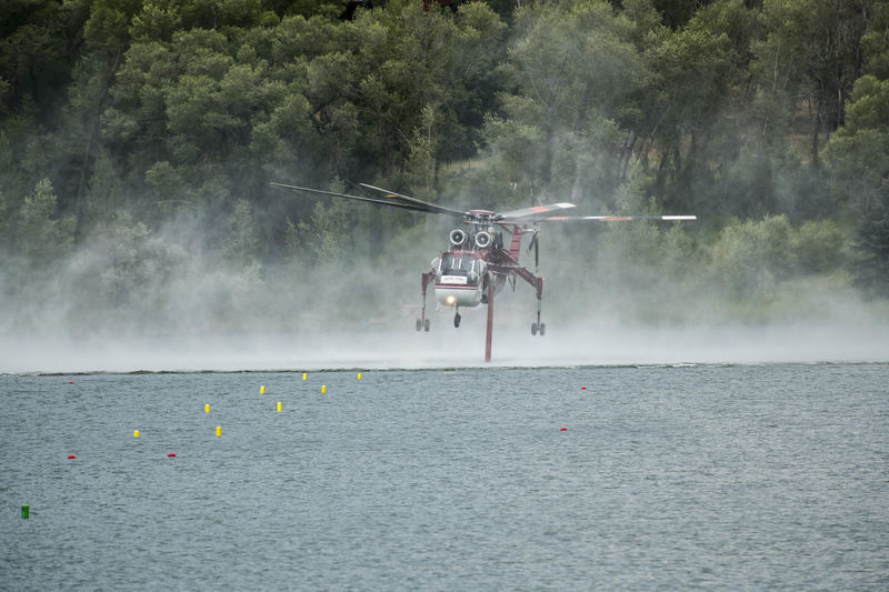 Military helicopter flying over lake while smoke emitting from wildfire in background