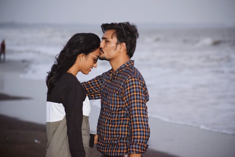 Side view of boyfriend kissing on girlfriend forehead at beach