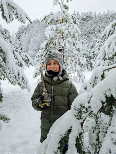 Portrait of boy standing amidst snow covered trees